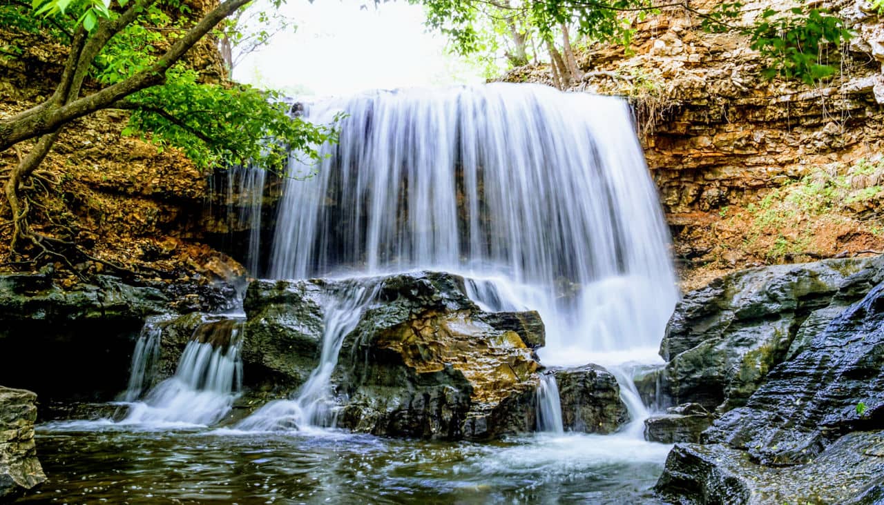 Waterfall cascading over a rocky ledge in Ardmore, GA with white water flowing down layered stone and green trees above.