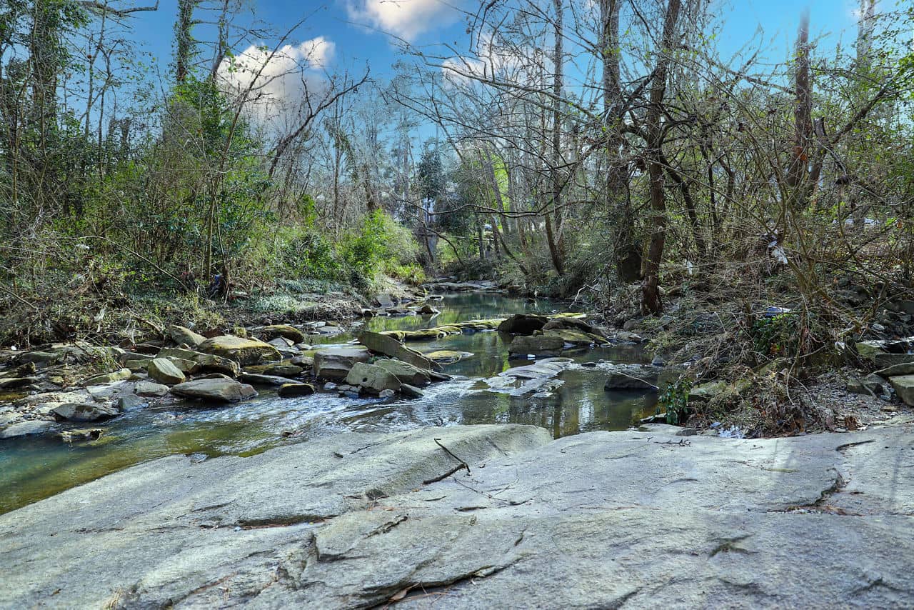 Rocky creek flowing through Buckhead Village, GA with a flat stone bed, shallow water, and early spring trees.