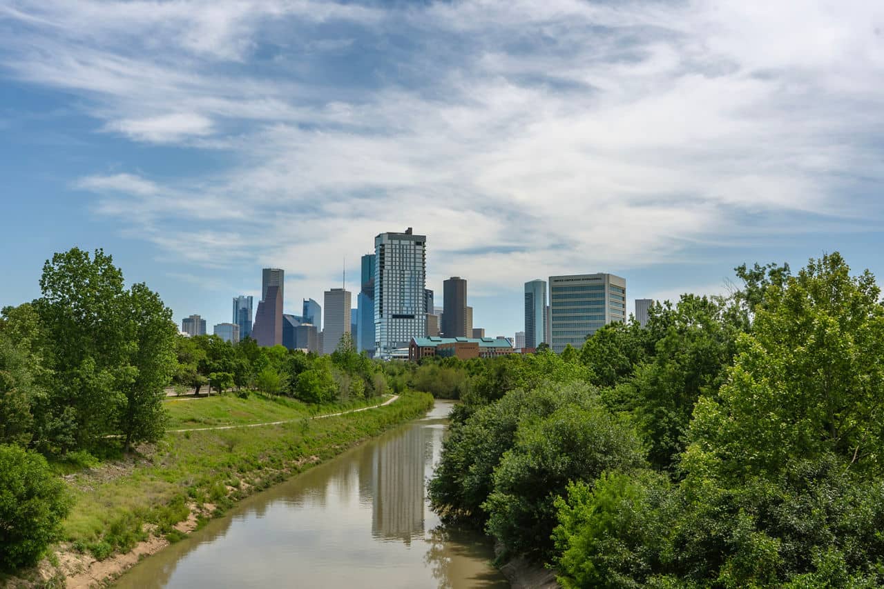 A view of the Greenway/Upper Kirby neighborhood in Houston, Texas, featuring a river and tall buildings in the background.